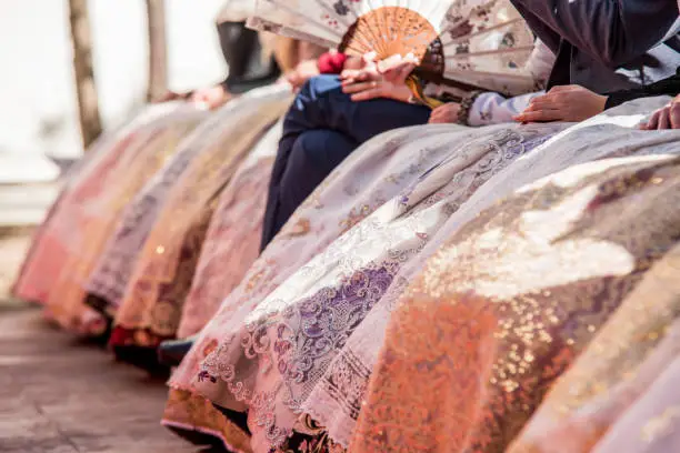 Photo of Fallera dresses, bright colors and reflections in these typical costumes of the fallas of Valencia. Falleras seated in a public act.