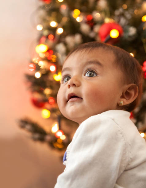 istock Baby girl with the Christmas tree behind her 1280198662