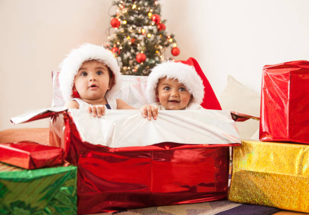 Beautiful babies inside a box wrapped as a Christmas present and wearing Santa hats - holidays concepts