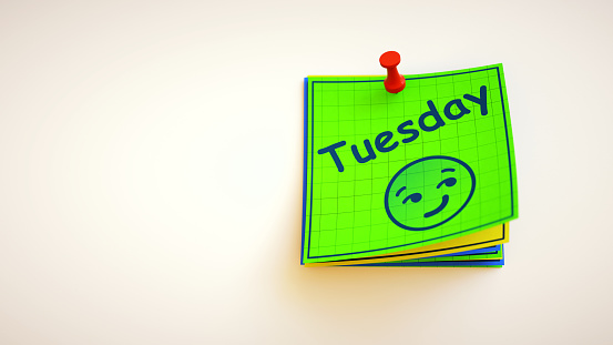 A stack of simple colorful notes with a smiling face and the word Tuesday. With copy space for additional composition.