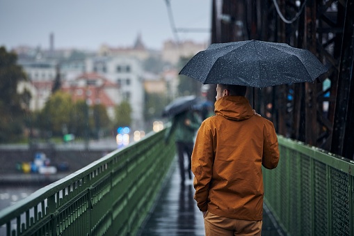 Young man with umbrella is walking on bridge during heavy rain. Gloomy day in Prague, Czech Republic