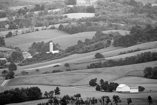 A monochrone image of the farms and farmland in among the fertile tree covered hills.