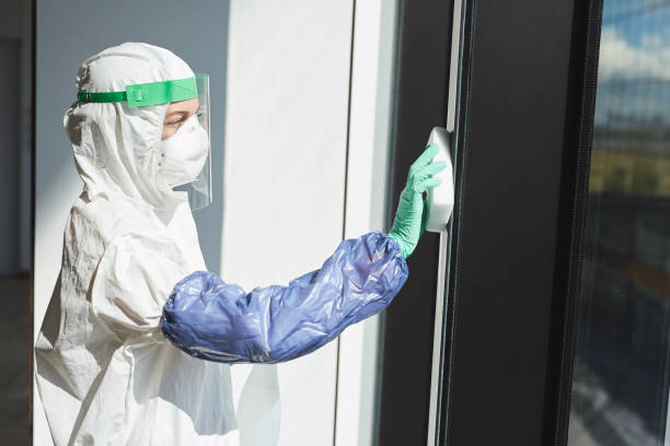 Cleaning Worker Washing Windows Side view portrait of female worker wearing hazmat suit disinfecting windows in office building, copy space biohazard cleanup stock pictures, royalty-free photos & images