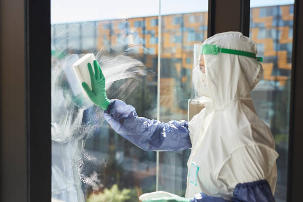 Professional Cleaning Worker Washing Windows Side view portrait of female worker wearing hazmat suit washing windows and disinfecting office in sunlight, copy space biohazard cleanup stock pictures, royalty-free photos & images