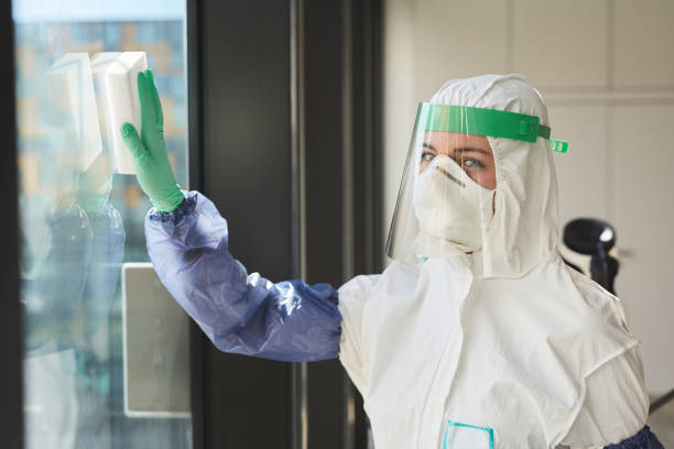 Female Cleaning Worker Washing Windows Waist up portrait of female worker wearing hazmat suit looking at camera while washing windows and disinfecting office, copy space cleanroom photos stock pictures, royalty-free photos & images