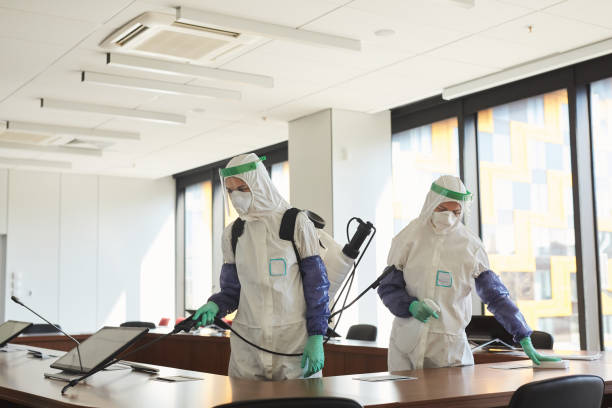 Two People Disinfecting Office Wide angle portrait of two sanitation workers wearing hazmat suits cleaning and disinfecting conference room in office, copy space biohazard cleanup stock pictures, royalty-free photos & images