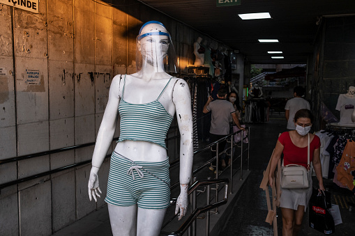 Izmir, Turkey 30/09/2020: A mannequin with a face mask at the entrance of a bazaar in Konak district. People are walking around for shopping in evening.