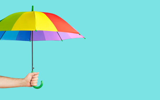 istock Rainbow-colored umbrella in male hand on green background 1280208614