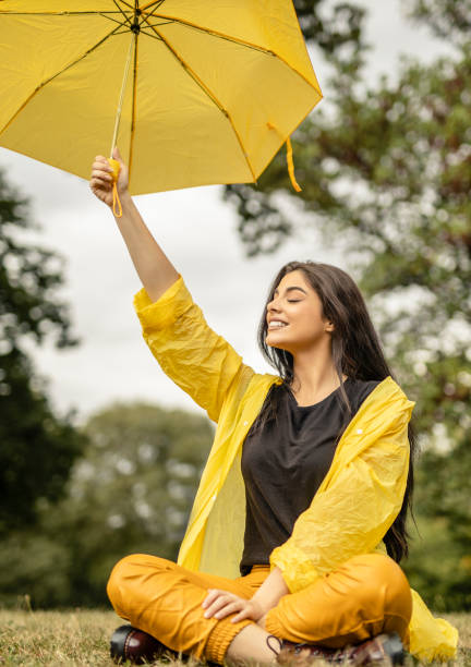 黄色いレインコートを着て、屋外で黄色い傘を持っている美しい若い女性 - umbrella women storm yellow ストックフォトと画像