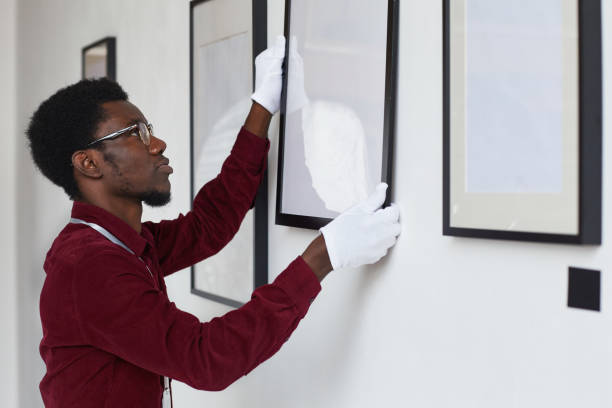 istock Worker Hanging Paintings on Wall in Museum Side View 1280209540