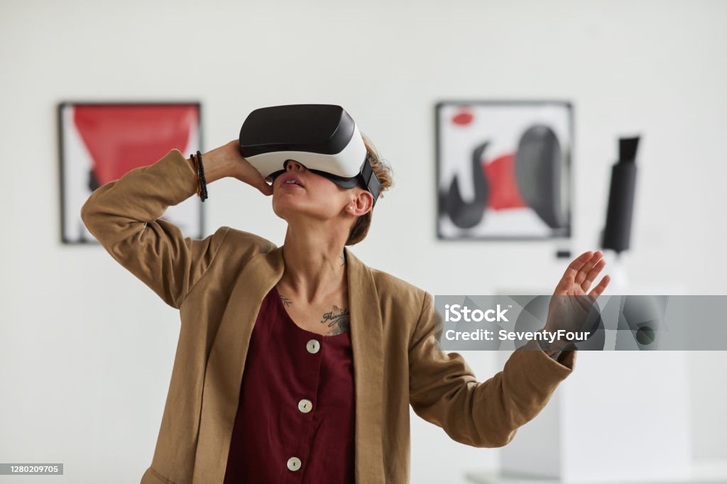 Young Woman Wearing VR in Museum of Modern Art Graphic waist up portrait of modern young woman wearing VR gear while enjoying immersive experience at art gallery exhibition Virtual Reality Stock Photo