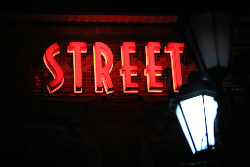 word Street glowing in red on a dark wall by a street lamp