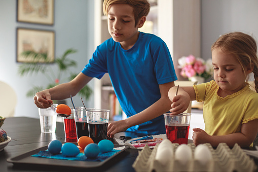 Front view of hardworking siblings putting Easter eggs in colorful inks to decorate the house during season.