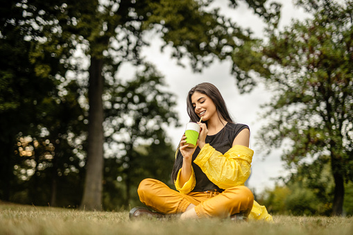 Young beautiful woman sitting on grass and drinking coffee
