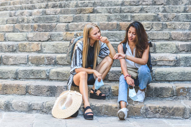 deux jeunes femmes attrayantes assis sur des escaliers en pierre et de vérifier l’heure sur leur montre - checking the time watch women looking photos et images de collection