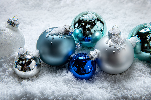 This is a photograph of blue and white and Silver Christmas ornaments shot in the snow. There are no people in the photograph