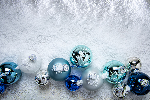 This is a photograph of blue and white and Silver Christmas ornaments shot in the snow on a white wooden background. There are no people in the photograph