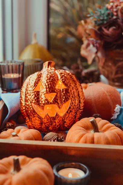 Close up Halloween cozy mood composition on the windowsill. Lighting jack-o-lantern, decorative pumpkins, cones, candles on wooden tray near window. Hygge halloween home decor. Selective focus. de cerca halloween acogedor composición de humor en el alféizar de la ventana. iluminación jack-o-lantern, calabazas decorativas, conos, velas en bandeja de madera cerca de la ventana. hygge halloween decoración para el hogar. enfoque selectivo