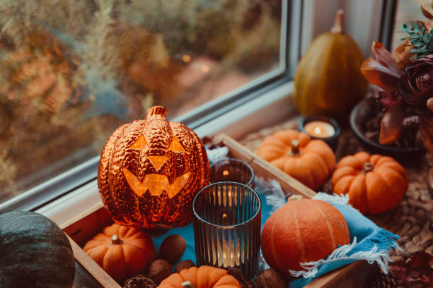 istock Halloween cozy mood composition on the windowsill. Lighting jack-o-lantern, decorative pumpkins, cones, candles on wooden tray and straw napkin, warm plaid. Hygge halloween home decor. Selective focus 1280221500