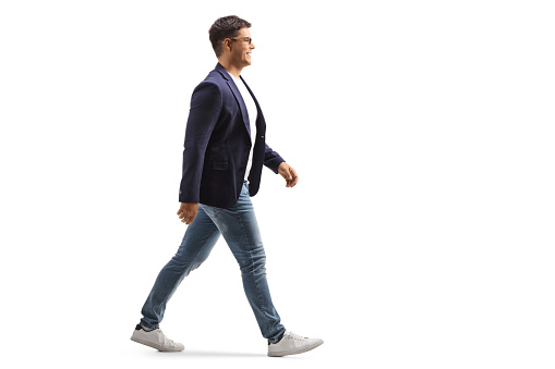 Toma de perfil de longitud completa de un joven sonriente en jeans y traje caminando photo