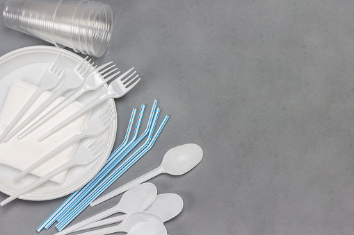Disposable white plastic tableware. Plate, spoons, forks, straws for drinks. Plastic processing problem. Ecology environmental care. Flat lay. Grey background. Copy space
