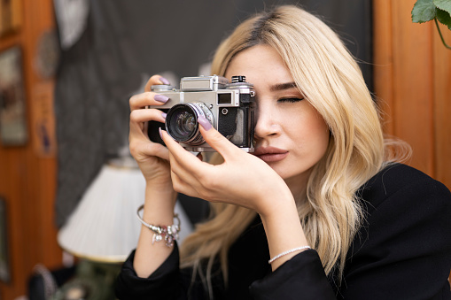 Half length of beautiful blonde woman outdoor in the city holding instant camera, shooting - photography, creative, artist concept. obscured view of fashionable man taking picture on vintage retro photo camera.