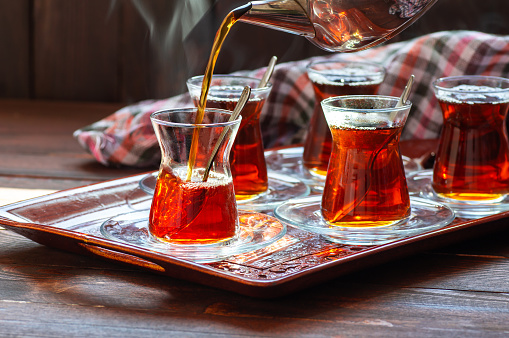 Glass cup of brewed black turkish tea pouring from teapot, traditional hot drink concept