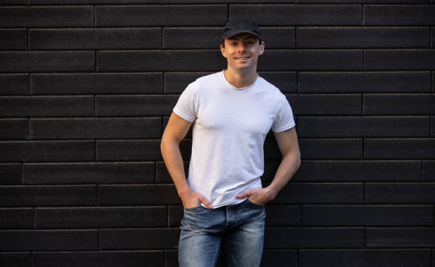 istock Smling man in white t-shirt standing against brick wall, mockup design 1280228667