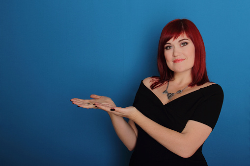 Portrait of white beautiful young woman pointing fingers with both hands aside, isolated in blue background.