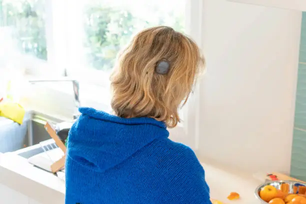 Photo of Adult female with cochlear implant cuts fresh oranges on kitchen counter