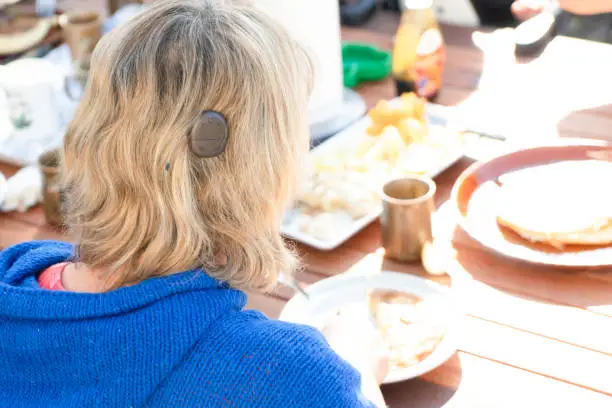 Photo of Adult female with cochlear implant having pancakes for breakfast outdoors with friends