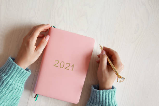woman sitting in knitted warm sweater with coral coloured 2021 diary on table - nature writing women ideas imagens e fotografias de stock