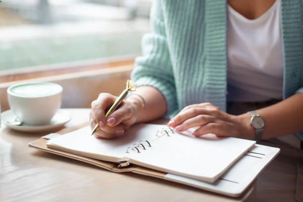 well groomed woman hand holding gold pen and writing notes with gold pen in notebook beside window - nature writing women ideas imagens e fotografias de stock