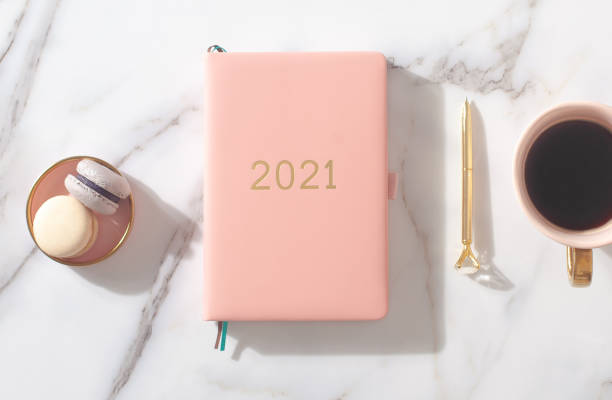 Pink coral colored diary for the year 2021, pen, coffee, macaron cookie. Marble background