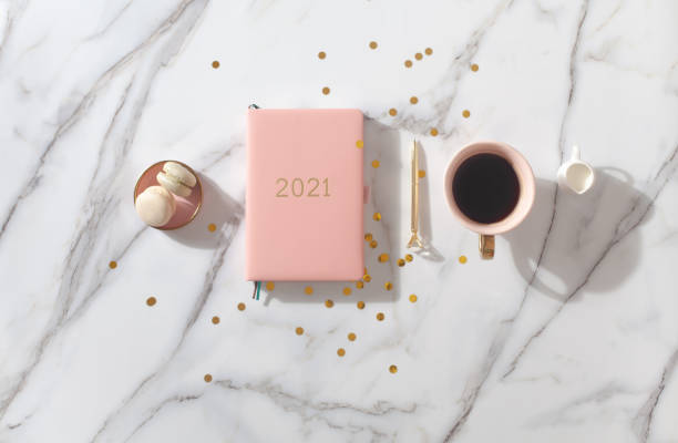 pink coral colored diary for the year 2021, pen, coffee, macaron cookie. marble background - copy space single object confetti nobody imagens e fotografias de stock