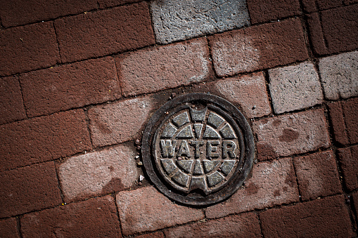 Stock photo of water main cover on brick sidewalk.