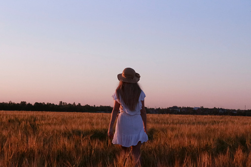a beautiful girl in a short summer dress runs through a field of rye. she has long hair through which the sun shines