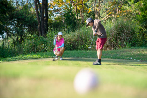 couple golf player putting golf ball on the green golf.  asia man and woman putting golf ball on tee with club in golf course on evening on time for healthy sport. lifestyle and sport concept - golf golf swing putting cheerful imagens e fotografias de stock