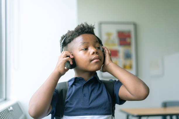 verticale du garçon mignon d’âge élémentaire écoutant la musique à l’école - différence dâge photos et images de collection