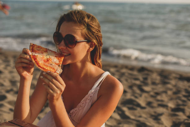 istock Woman eating pizza by the beach 1280247323