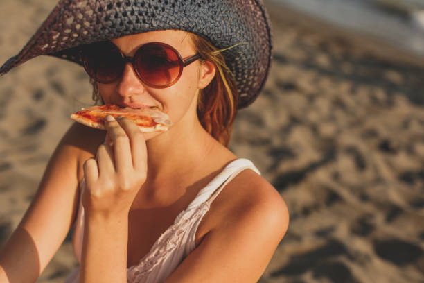 istock Woman eating pizza by the beach during sunny afternoon 1280247337