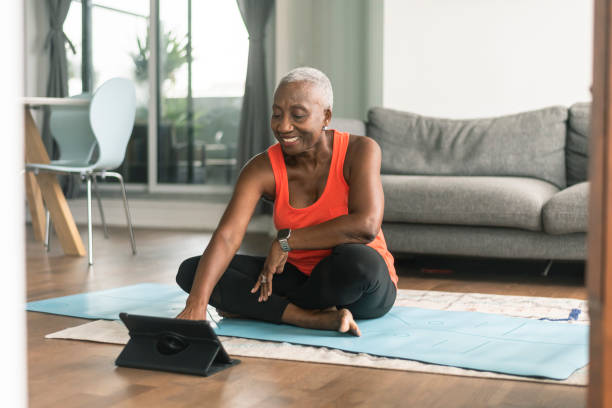 una mujer negra mayor toma una clase de yoga en línea - relaxation exercise yoga exercising women fotografías e imágenes de stock