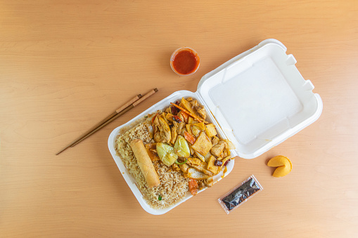 Chinese takeaway food, in a disposable container with fried rice, chicken, vegetables, Chinese sticks and soy sauce and siracha