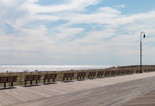 The Long Beach New York boardwalk with a long row of empty wood benches facing the beach with the ocean
