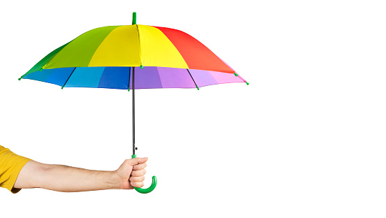 Close-up of a cute little girl with curly red hair holding a rainbow colored umbrella behind her on a rainy day. Her hair is wet from playing in the rain. She is smiling at the camera.