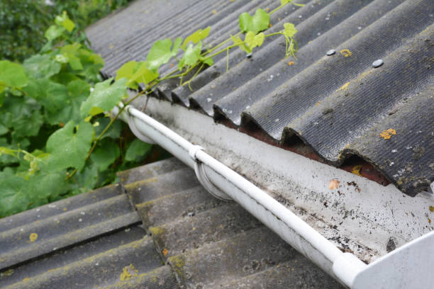 istock A plastic rain gutter on an asbestos rooftop is cleaned from fallen leaves, dirt and other debris to avoid water overflowing from gutter and protect the house from water damage. 1280280590