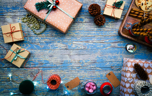 Directly above view of presents with food and decorations. Top view of various objects are on blue table. Image represents Christmas season.