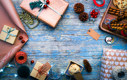 Above view of presents with food and decorations. Various objects are on blue table. Image represents Christmas season.