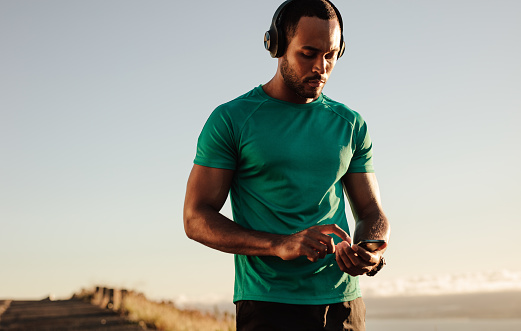 Portrait of an athlete using mobile phone during morning run. Athletic man listening to music on wireless headphones.
