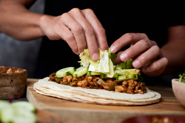 man preparing a durum or a burrito closeup of a young caucasian man preparing a durum or a burrito, with chicken meat cooked with different vegetables such as onion or red and green pepper, and fresh lettuce and raw cucumber making a sandwich stock pictures, royalty-free photos & images